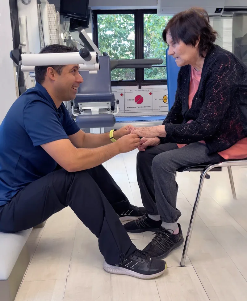 Kinesiólogo atendiendo a paciente adulta mayor durante ejercicio asistido en clínica de kinesiología en La Reina