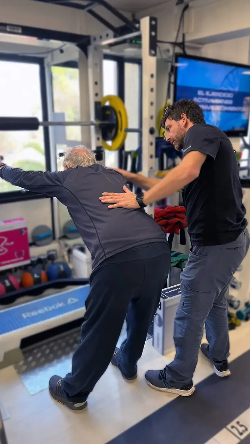 Kinesiólogo profesional asistiendo a paciente adulto mayor durante ejercicio de elongación y estiramiento terapéutico en KinesicWork